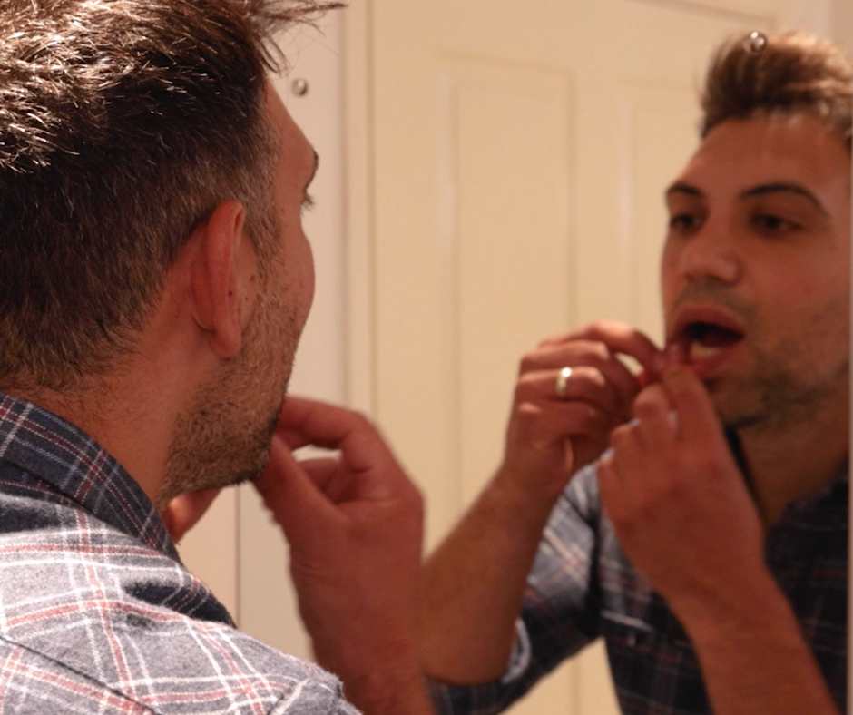 man standing in front of mirror gently lifting his lips with his fingers to inspect his gums