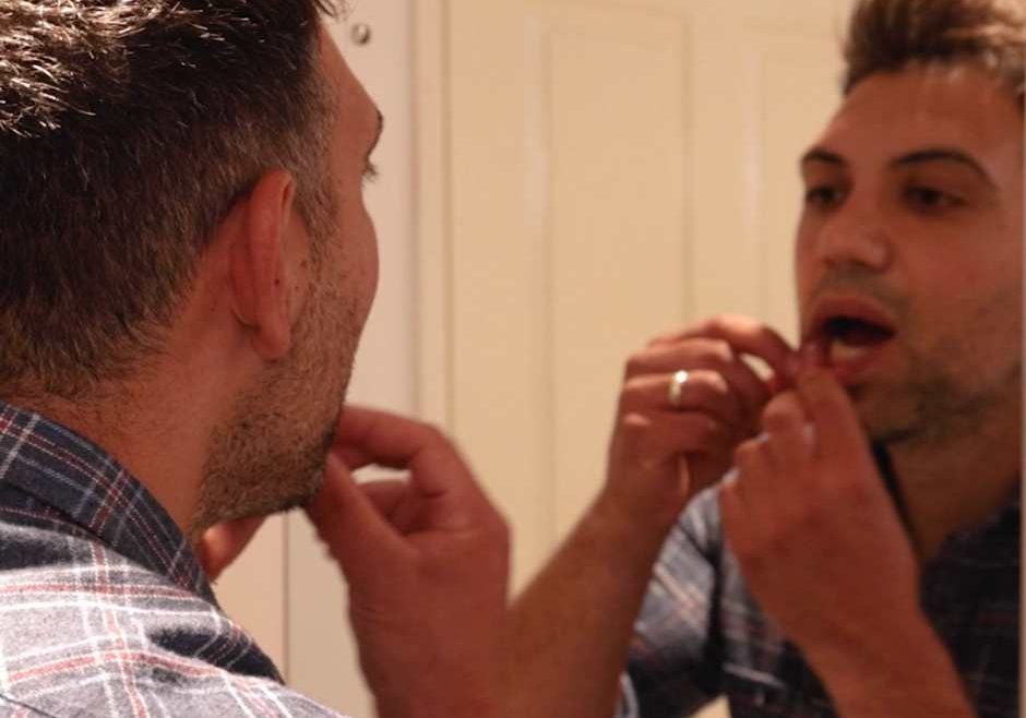 man standing in front of mirror gently lifting his lips with his fingers to inspect his gums